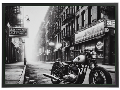 Et sort-hvidt billede af en vintage motorcykel parkeret på en stille gade med tåge.