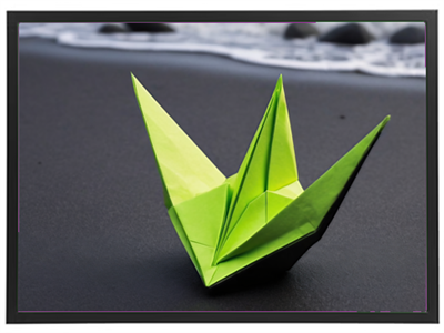 En detaljeret origami fuglefigur i grønt papir, placeret på en mørk sandstrand med vand i baggrunden.