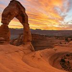 Delicate Arch i Arches National Park med en farverig solnedgang i baggrunden.