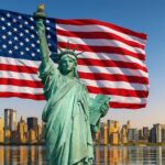 Statue of Liberty med det amerikanske flag i baggrunden og skyline af New York City.